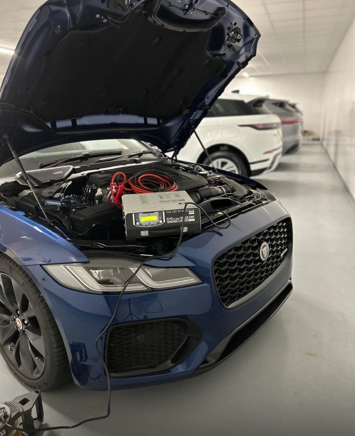 Luxury SUV engine bay with battery charger — automotive service work by Mileage Tuner